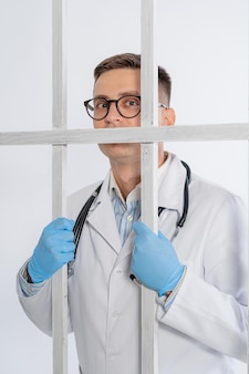 Человек в синих медицинских перчатках положил руки на железную белую клетку. врачи в качестве пленных из-за пандемии. трудные времена для медиков при эпидемии. крупный план.