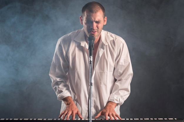 Бесплатное фото Человек в белой рубашке играет на клавишных и поет эффект дыма