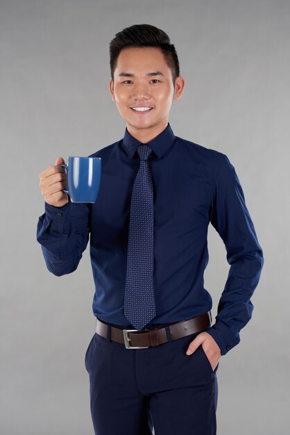 Man indark blue formalwear standing against grey background with navy blue mug of tea