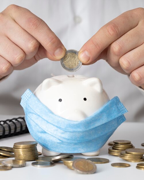 Man Inserting A Coin In A Piggy Bank With A Medical Mask