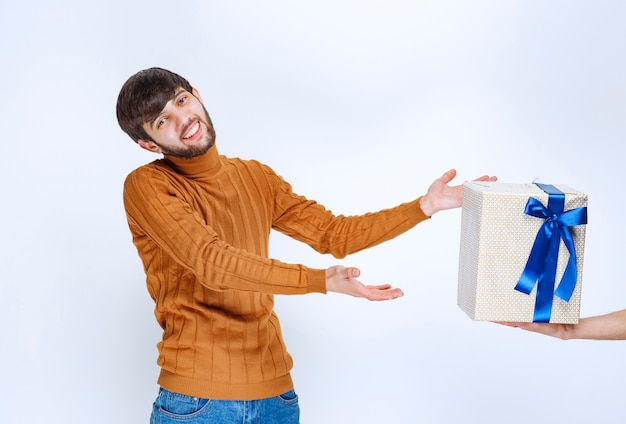Мужчине предлагают белую подарочную коробку с голубой лентой, и он берет ее обеими руками.
