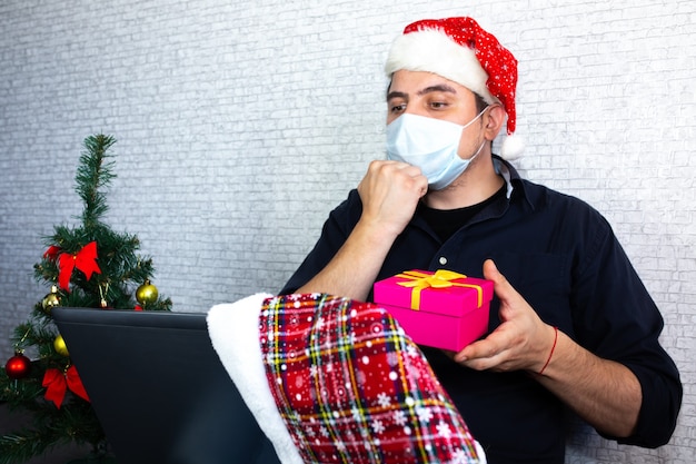 남자는 수화를 통해 의사 소통하고 있습니다. 노트북 근처에 산타 모자를 쓴 남자가 화상 통화를 통해 상호 작용하고 있습니다. 장애와 함께 살고 있습니다. 집에서 고립된 크리스마스. 휴가철 사회적 거리두기.
