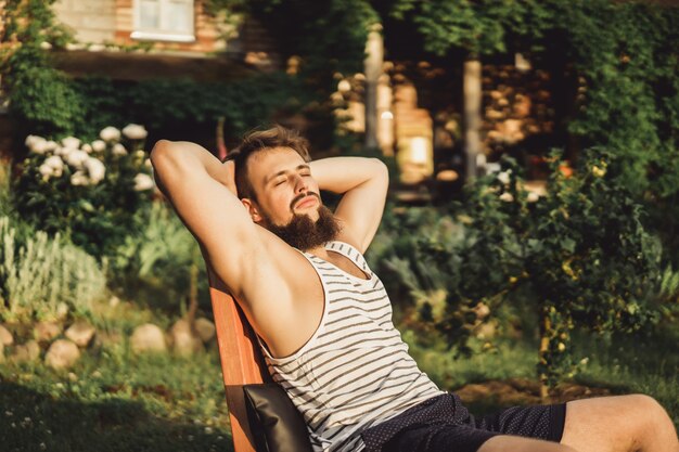 男はカントリーハウスで休んでいます。ひげのある男は緑の芝生の上で日没を楽しむ。