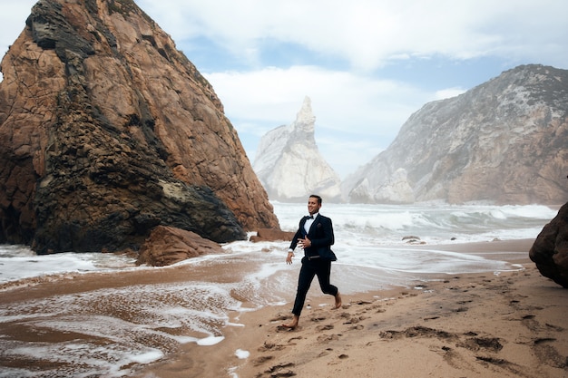 Man is running on the wet sand among the rocks