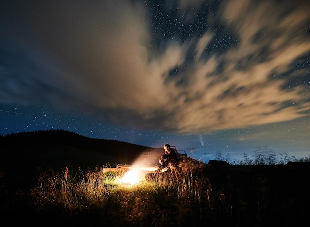 Man is sitting near bonfire in mountains in evening