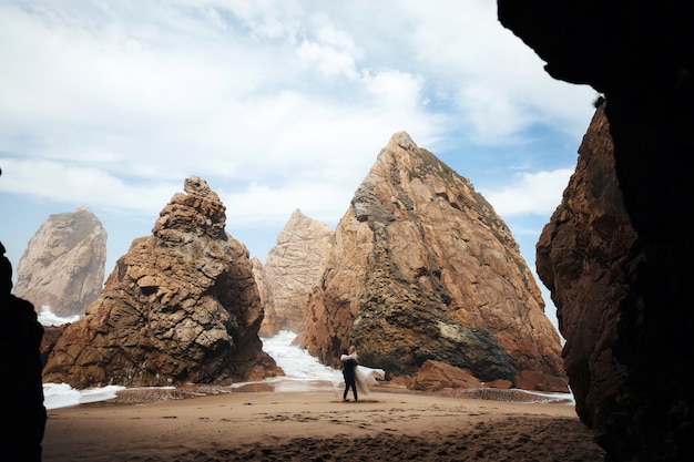 Free photo man is whirling the woman and they look very happiness, couple stand on the beach among the rocks