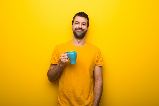 Man on isolated vibrant yellow color holding hot coffee in takeaway paper cup