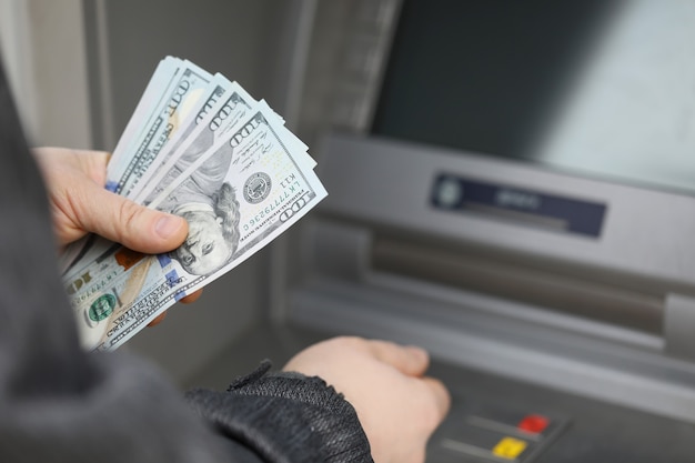 A man in a jacket holds dollars on the street near an atm secure password entry for cash