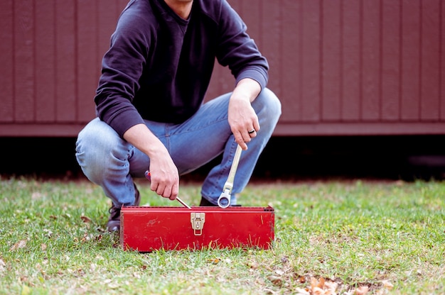 человек в джинсах держит гаечный ключ с красным ящиком для инструментов