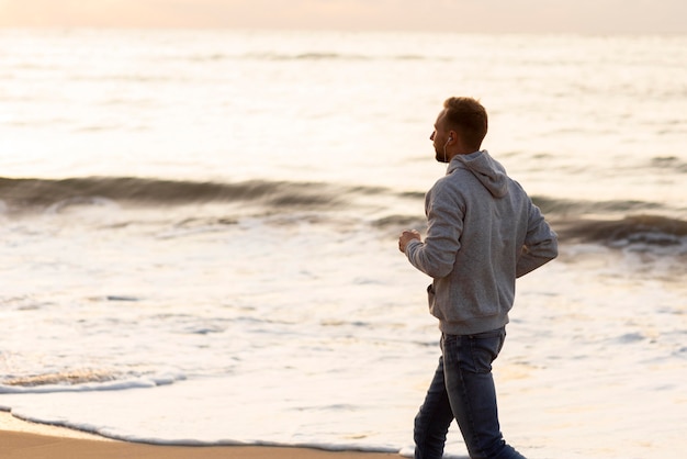 Free photo man jogging on the beach with copy space