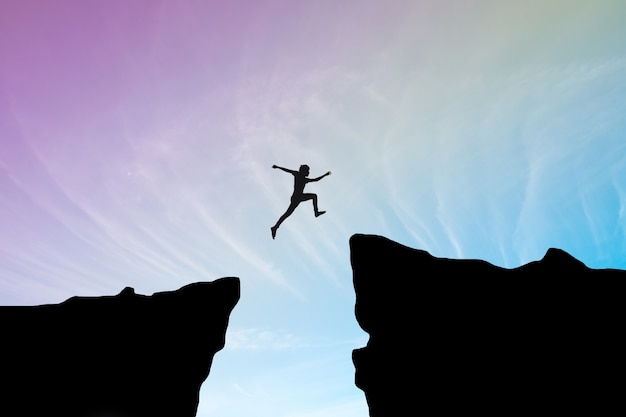 Человек прыгать через разрыв между hill.man прыгает через скалу на голубом небе, концепция концепции бизнеса