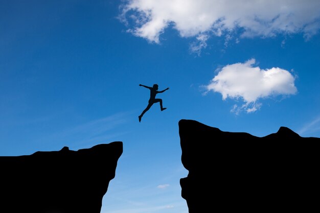 Человек прыгать через разрыв между hill.man, прыгать через скалы на фоне заката, идея концепции бизнеса