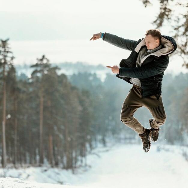 Man jumping outdoors in nature during winter and pointing to copy space