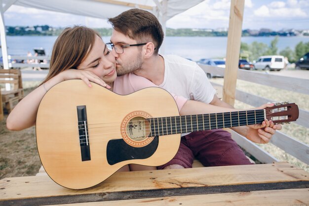 Мужчина целует девушку в лицо, и, опираясь на гитаре