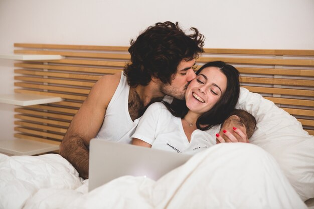 彼らはベッドの中でノートパソコンを見ながら、男は彼のガールフレンドにキス