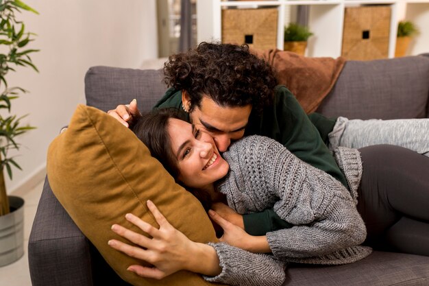 Man kissing his smiley wife while lying on the sofa