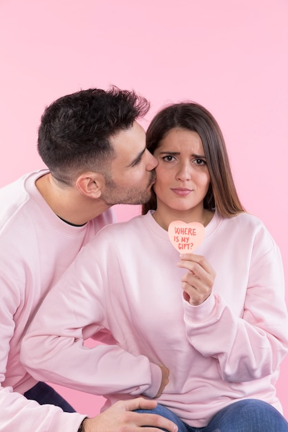 Man kissing serious young woman with paper heart