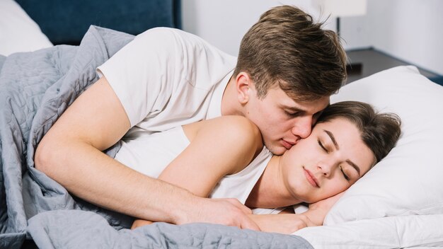 眠っている女性が頬にキスをする男性