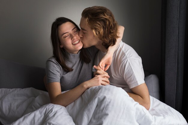 침대에서 웃는 여자 친구를 키스하는 남자