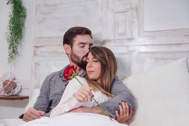 Мужчина целует женщину в лоб на кровати