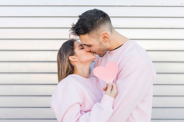 Man kissing woman holding decorative paper symbol of heart