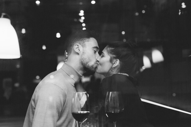 Мужчина целует женщину возле бокалов вина в ресторане