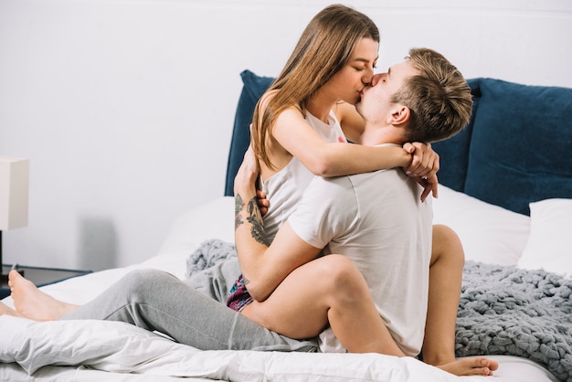 Man kissing woman sitting on bed