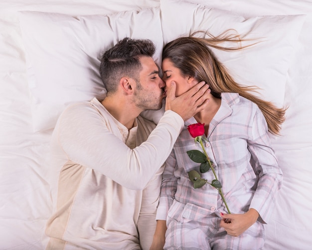 Man kissing woman with rose in bed 