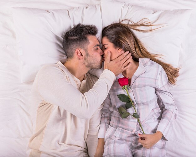 Мужчина целует женщину с розой в постели