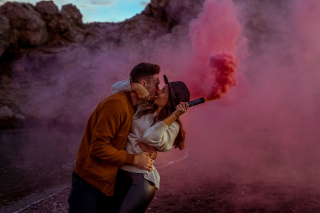 Foto gratuita equipaggi baciare la donna con la bomba fumogena sulla riva di mare