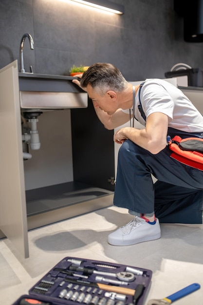 流しの下のパイプを検査するためにひざまずく男