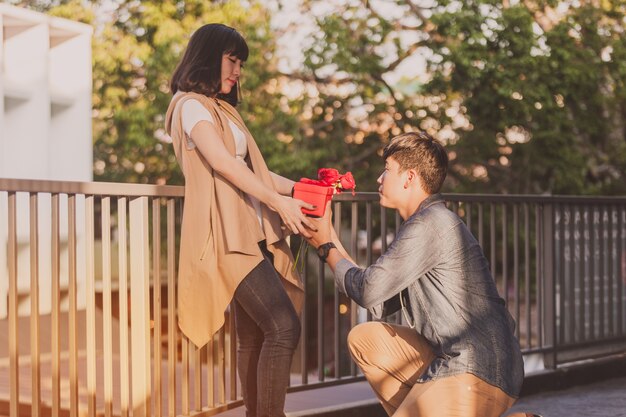 Man kneeling giving his girlfriend roses and a red gift