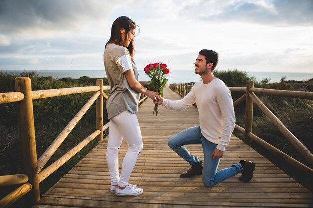 Free photo man kneeling handing a bouquet of roses to a woman