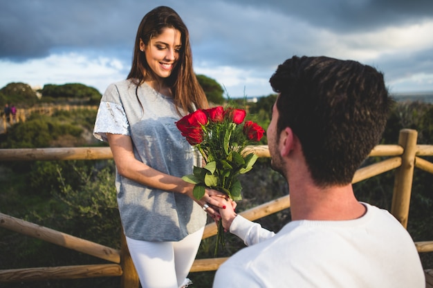 Man kneeling handing a bouquet of roses to a woman