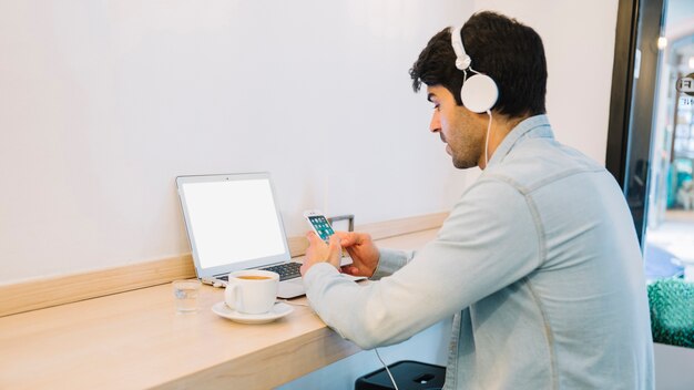 Man at laptop looking at smartphone