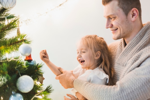 Man and laughing girl decorating illuminated christmas tree