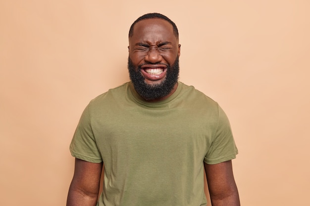 Free photo man laughs happily shows white perfect teeth dressed in casual t shirt poses on brown