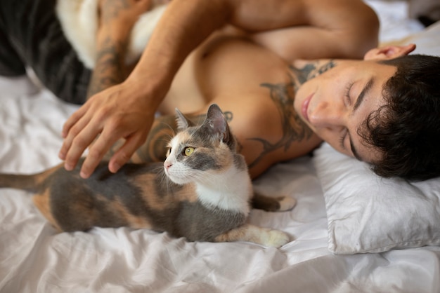 Мужчина лежит в постели с кошками под высоким углом