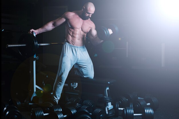 Man leaning on barbell and lifting dumbbell