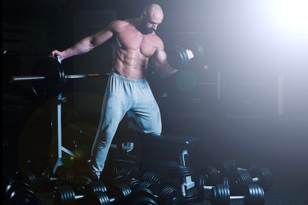 Man leaning on barbell and lifting dumbbell