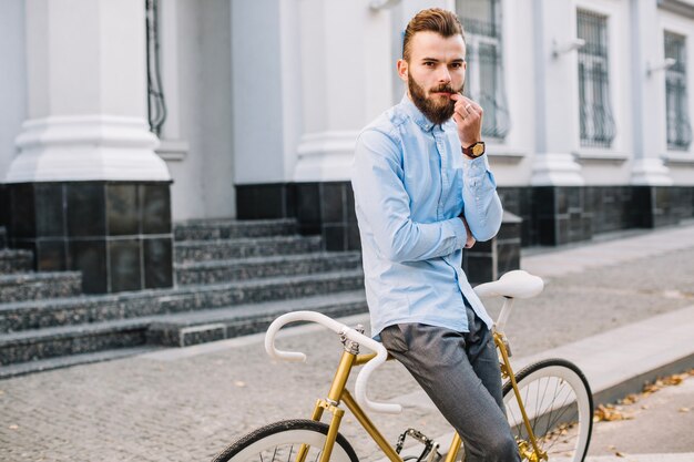 Man leaning on bicycle and touching moustache