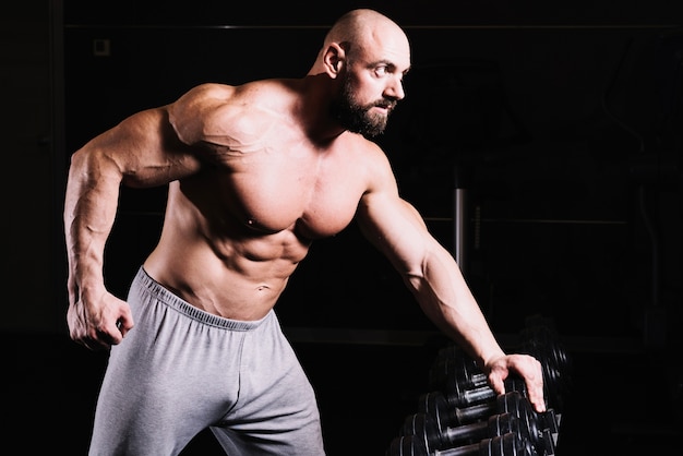 Free photo man leaning on dumbbell rack