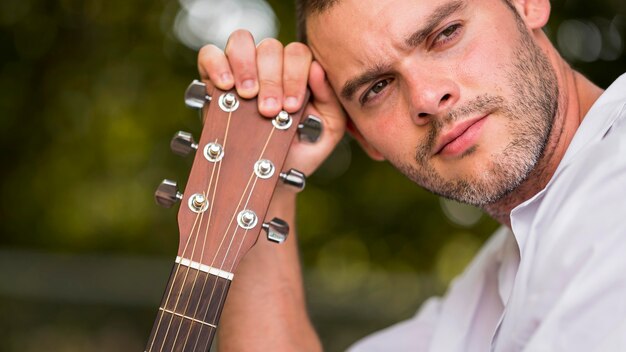 Man leaning his head on guitar headstock close-up