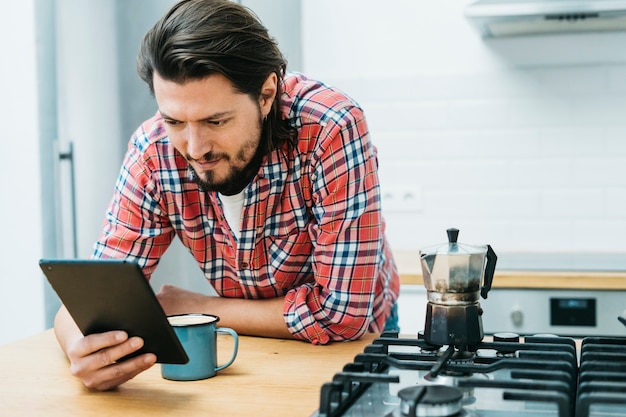 A man leaning on kitchen counter looking at smart phone