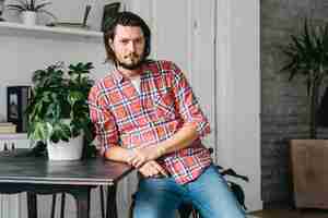 Free photo man leaning on table near the plant pot looking at camera