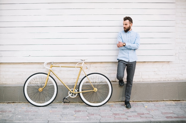 Uomo che si appoggia sulla parete bianca vicino alla bicicletta