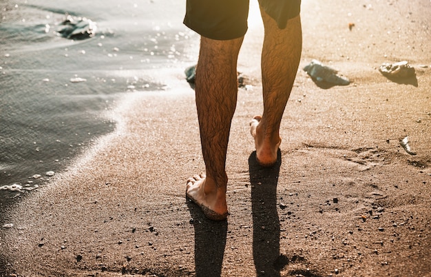 水の近くの砂の海岸に男の足