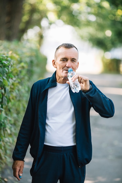 水を飲む口にボトルを持ち上げる男