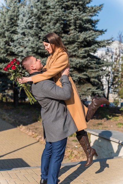 Free photo man lifting smiling woman with flowers