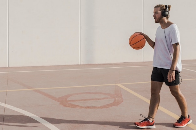 man listening to music on headphone walking with basketball in court